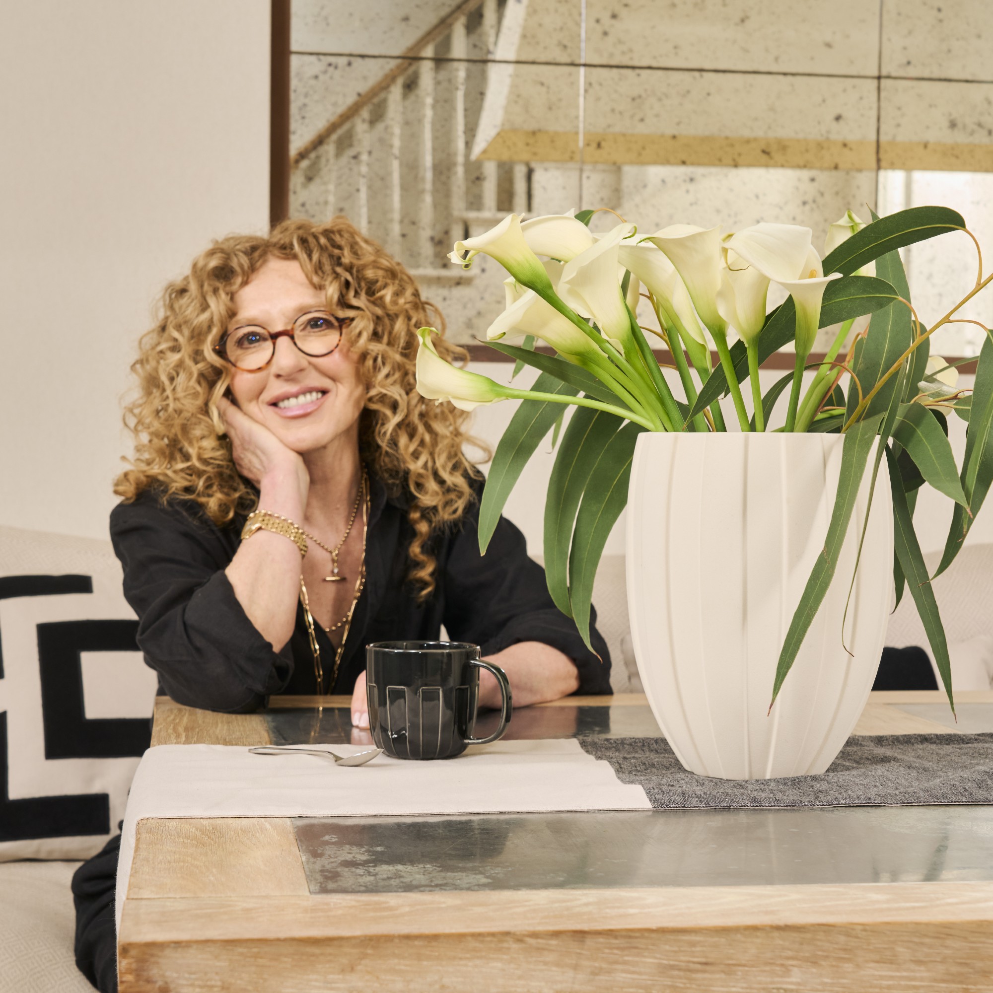 Kelly Hoppen sitting at a table with a vase of her M&amp;S calla lily bouquet next to her