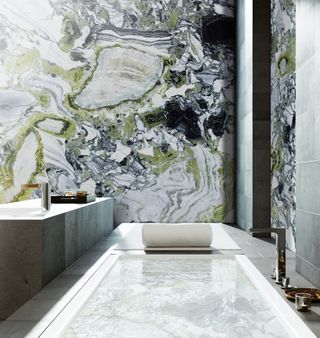 A bathroom with an inset bath and green, gray and black stone walls