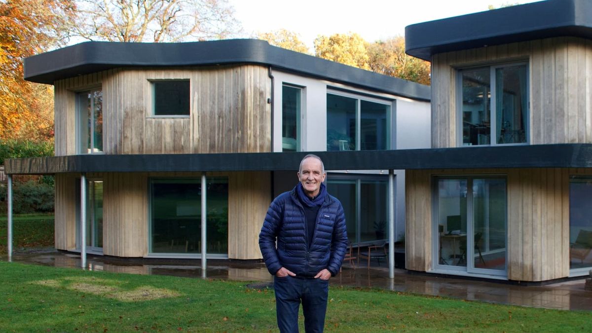 Kevin McCloud stood in front of a timber clad self build with a gap in the home