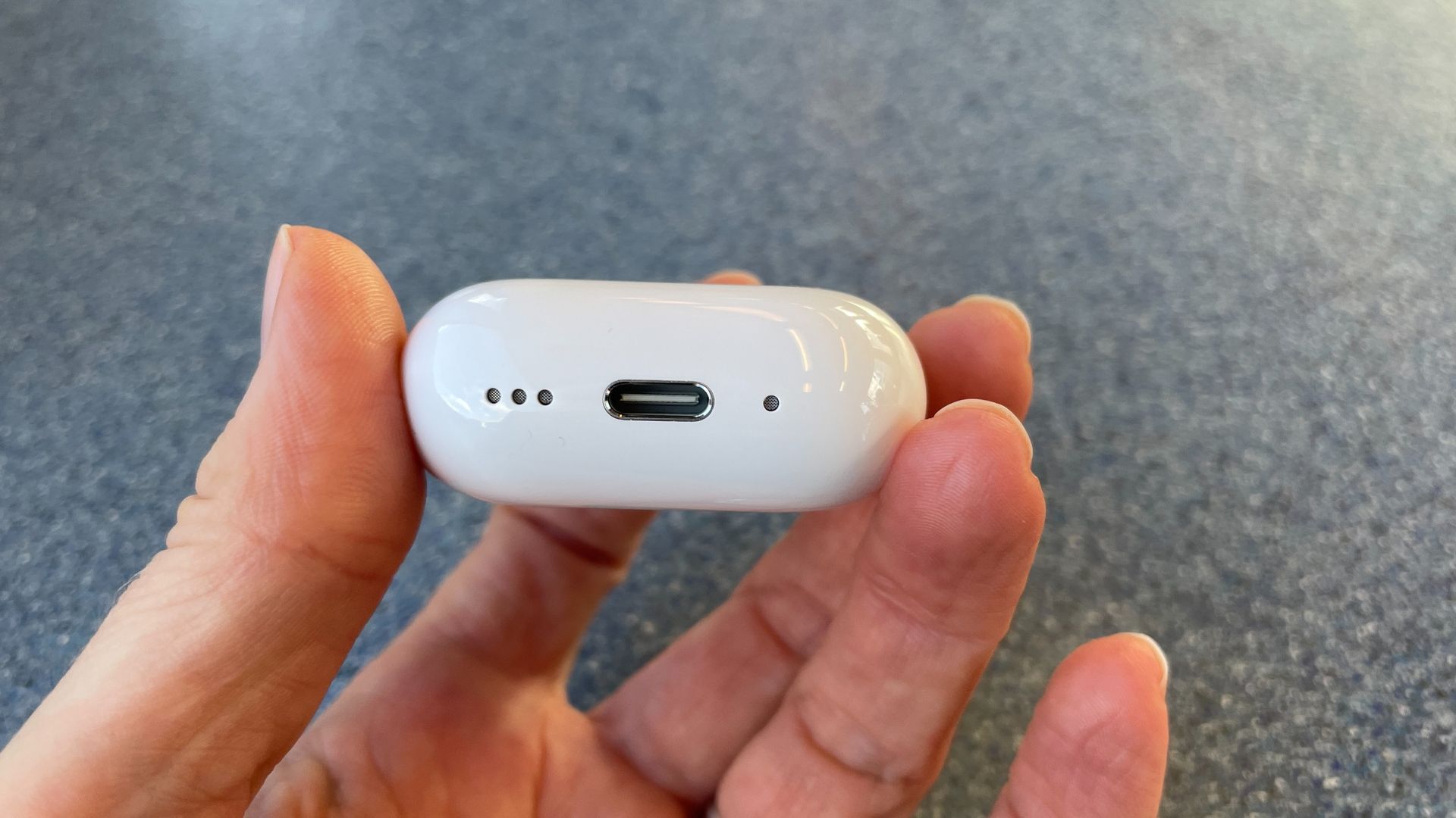 Apple AirPods 5 with Wireless Charging, on a blue table and held in a hand