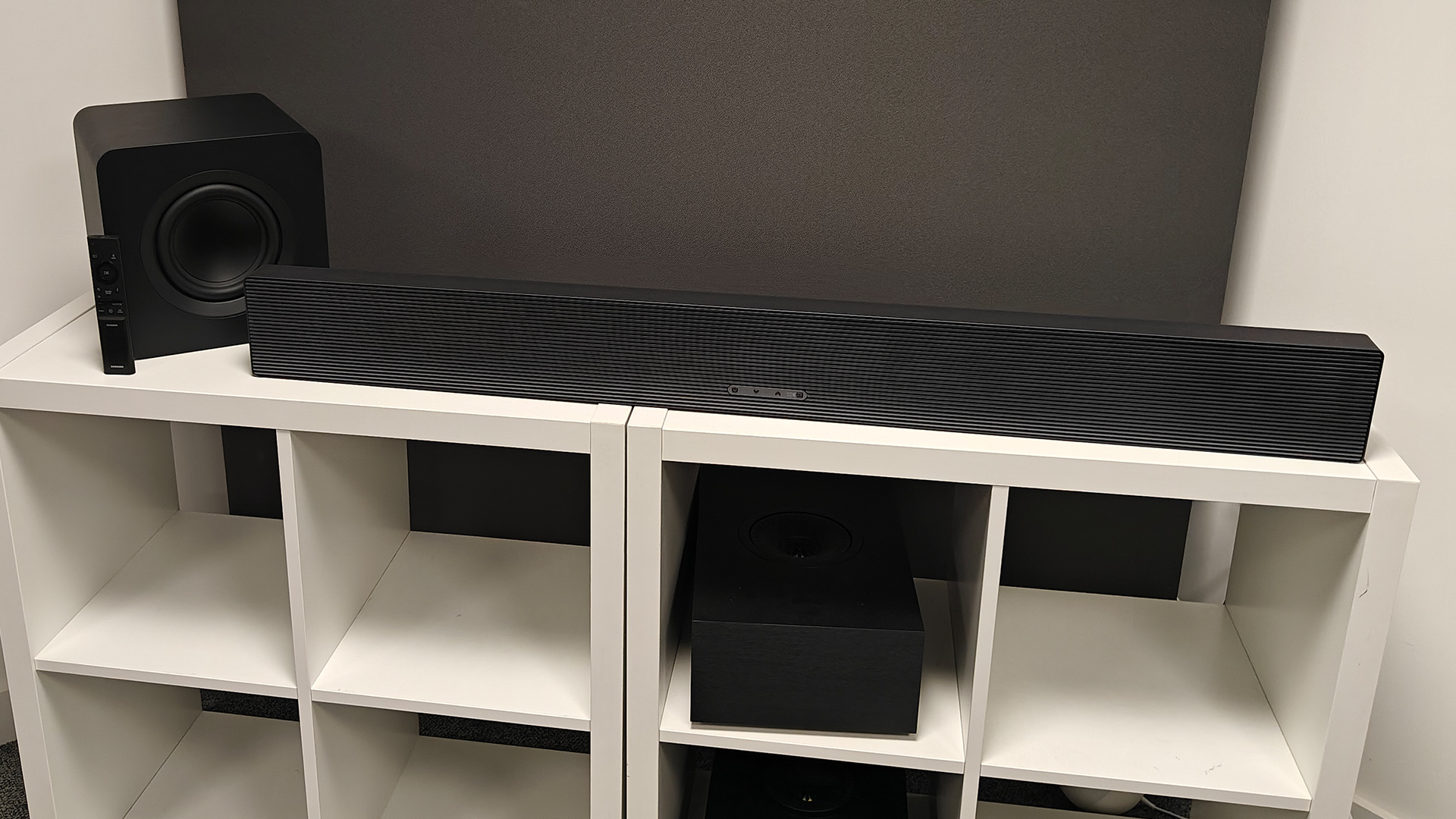 Samsung HW-QS700F Dolby Atmos soundbar on white shelf unit with subwoofer and remote