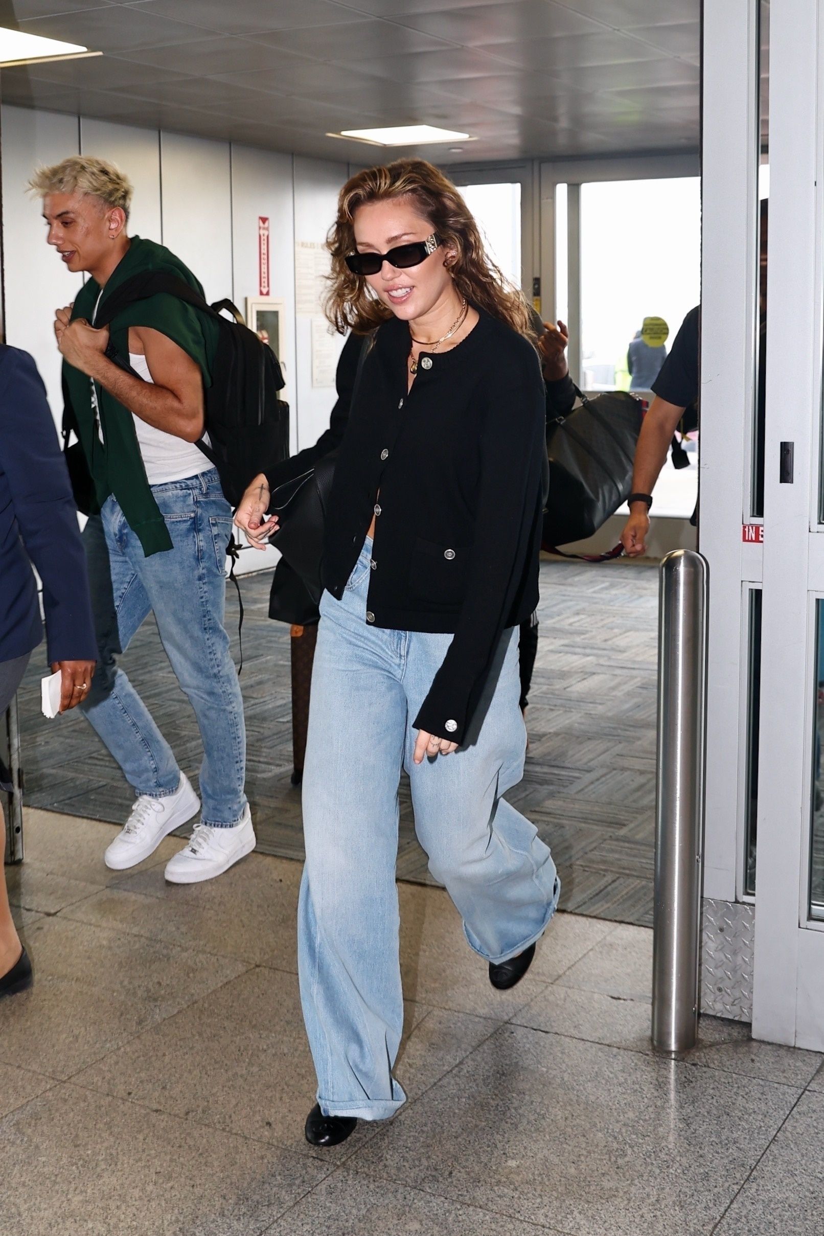 Miley Cyrus wears a pair of light-wash jeans with a black cardigan at the JFK airport.