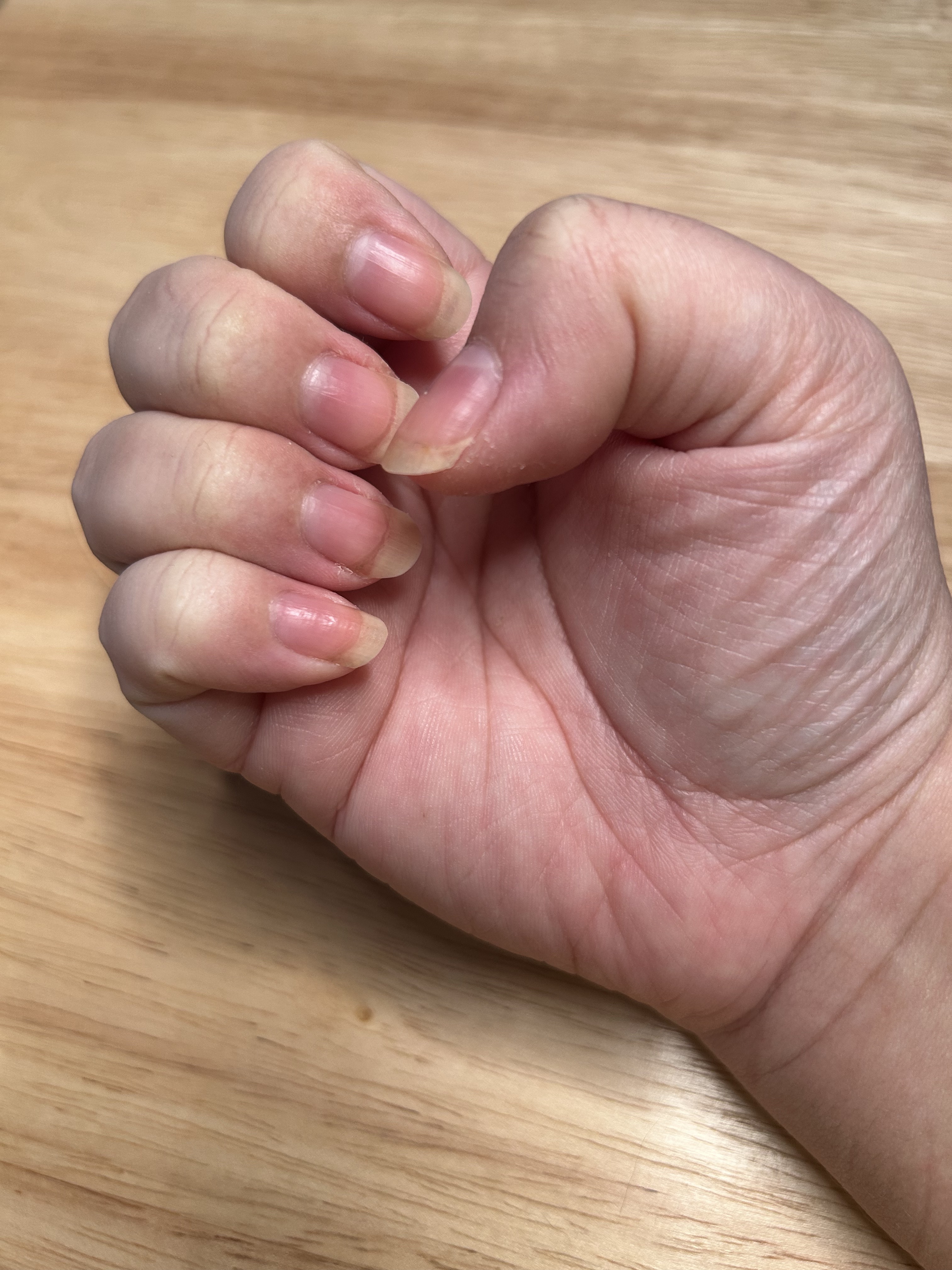 A woman's hand and nails before applying cuticle oil with a wood background.