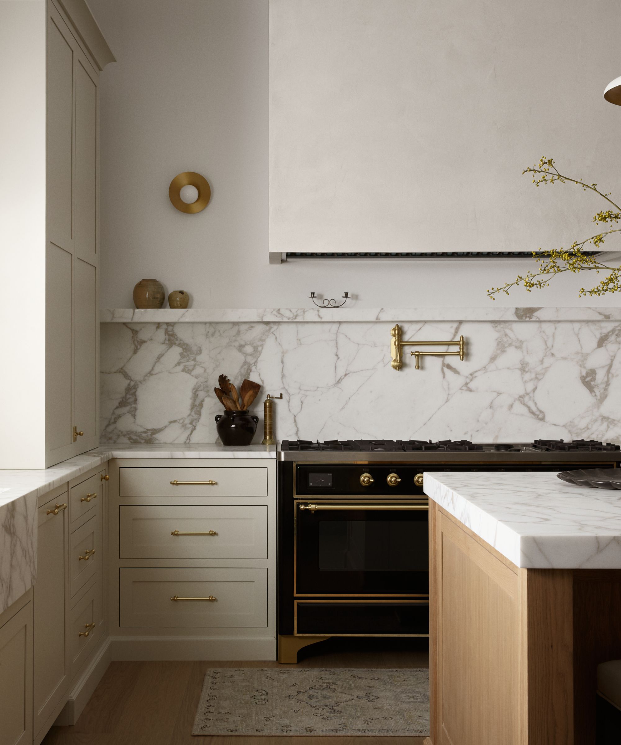 Close-up of a kitchen featuring a white marble backsplash and countertop, off-white drawers with brass handles, and a black and gold vintage-style range.
