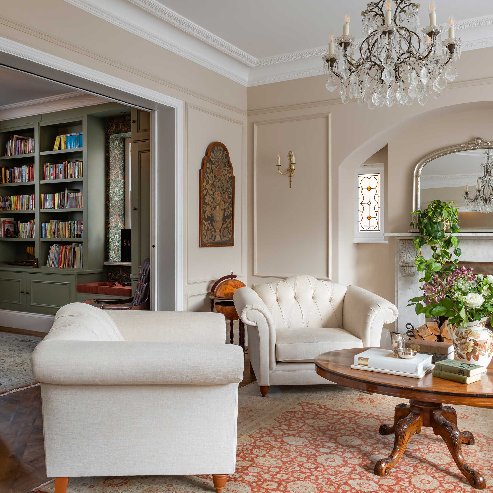 view of elegant living room in Edwardian home with antiques and chandelier leading into green painted library