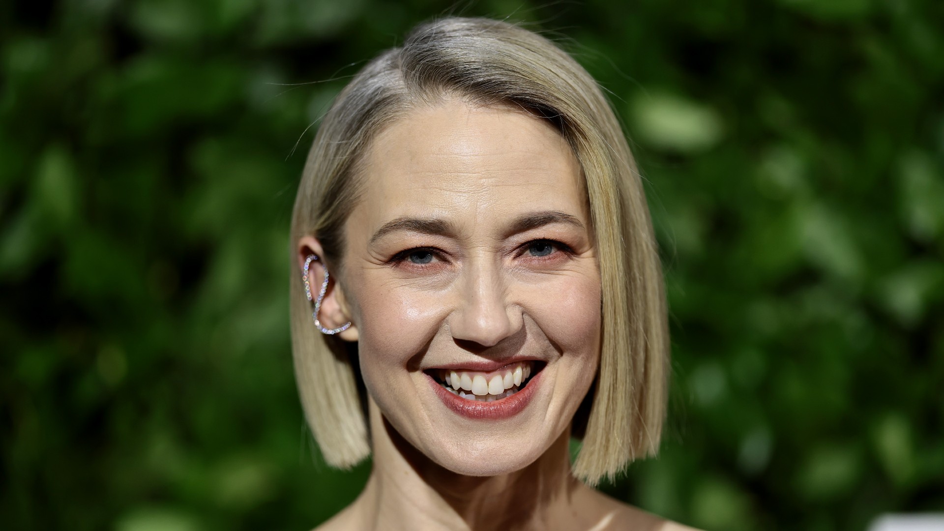 a headshot of a white woman with short hair posing in front of grassy background 