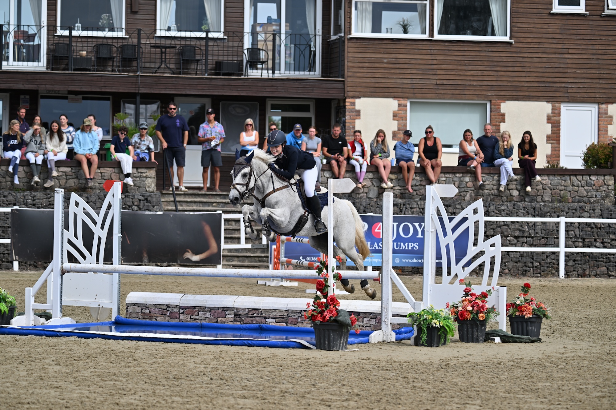 A young rider and a grey pony jumping an open water jump