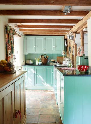 a country kitchen in a galley layout with blue/duck egg blue cabinets and wood worktops