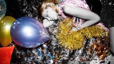 Woman lying asleep on the floor with party balloons, disco ball, and glittery tinsel 