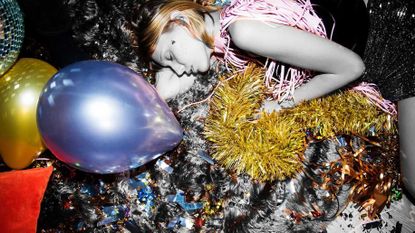 Woman lying asleep on the floor with party balloons, disco ball, and glittery tinsel 
