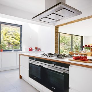white kitchen island with integrated oven, white walls and silver extractor fan
