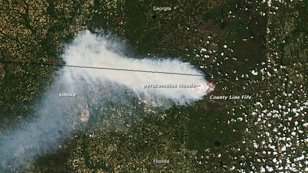 A plume of white smoke is seen over the green landscape of Earth from space