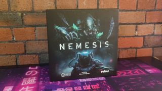 Nemesis box against a brick wall, on a neon mat