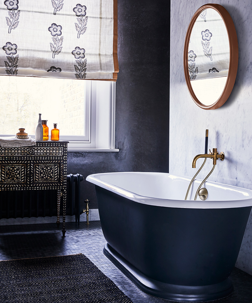 A black bathroom with a decorative storage cabinet under the window and block printed blinds