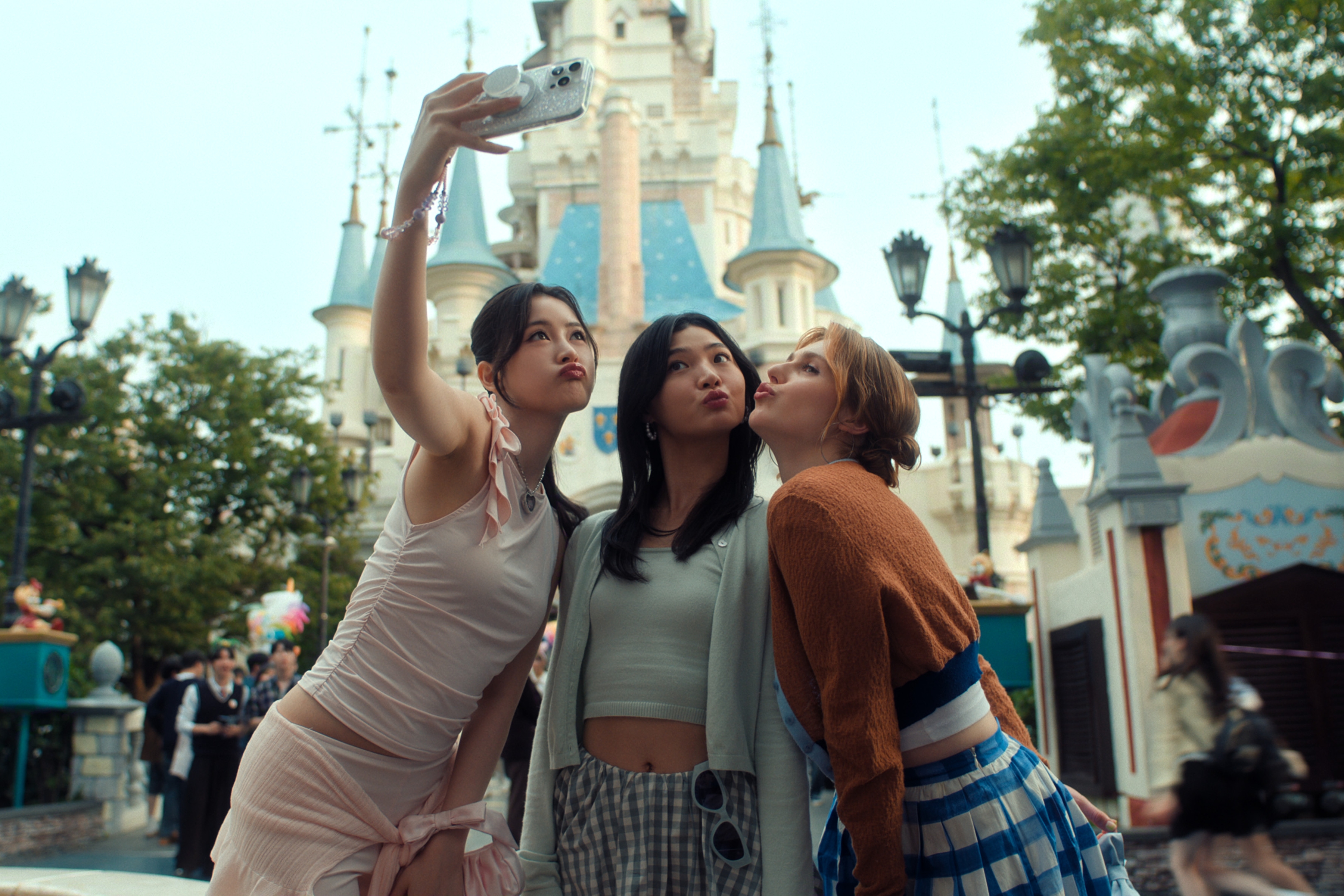 Han Bi Ryu as Eunice Kang, Sunny Oh as Mihee, Jocelyn Shelfo as Madison posing and making a face while taking a selfie together outside of the entrance to disney world seoul together in xo kitty season 3