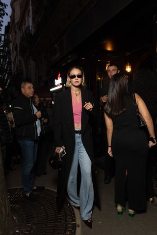 Gigi Hadid wears a black overcoat with a pink halter top and jeans