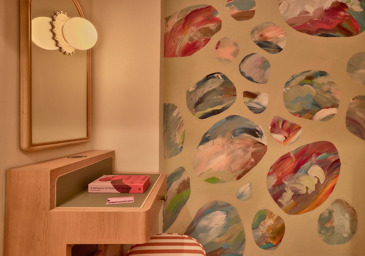 A vibrantly decorated hotel features murals-clad walls in pastel tones, wooden furniture, and Art Deco spherical lighting enriched with a goldeny base.