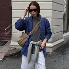 Annabel wears a blue jacket, gray t-shirt, white shorts, and a tan suede crossbody bag.