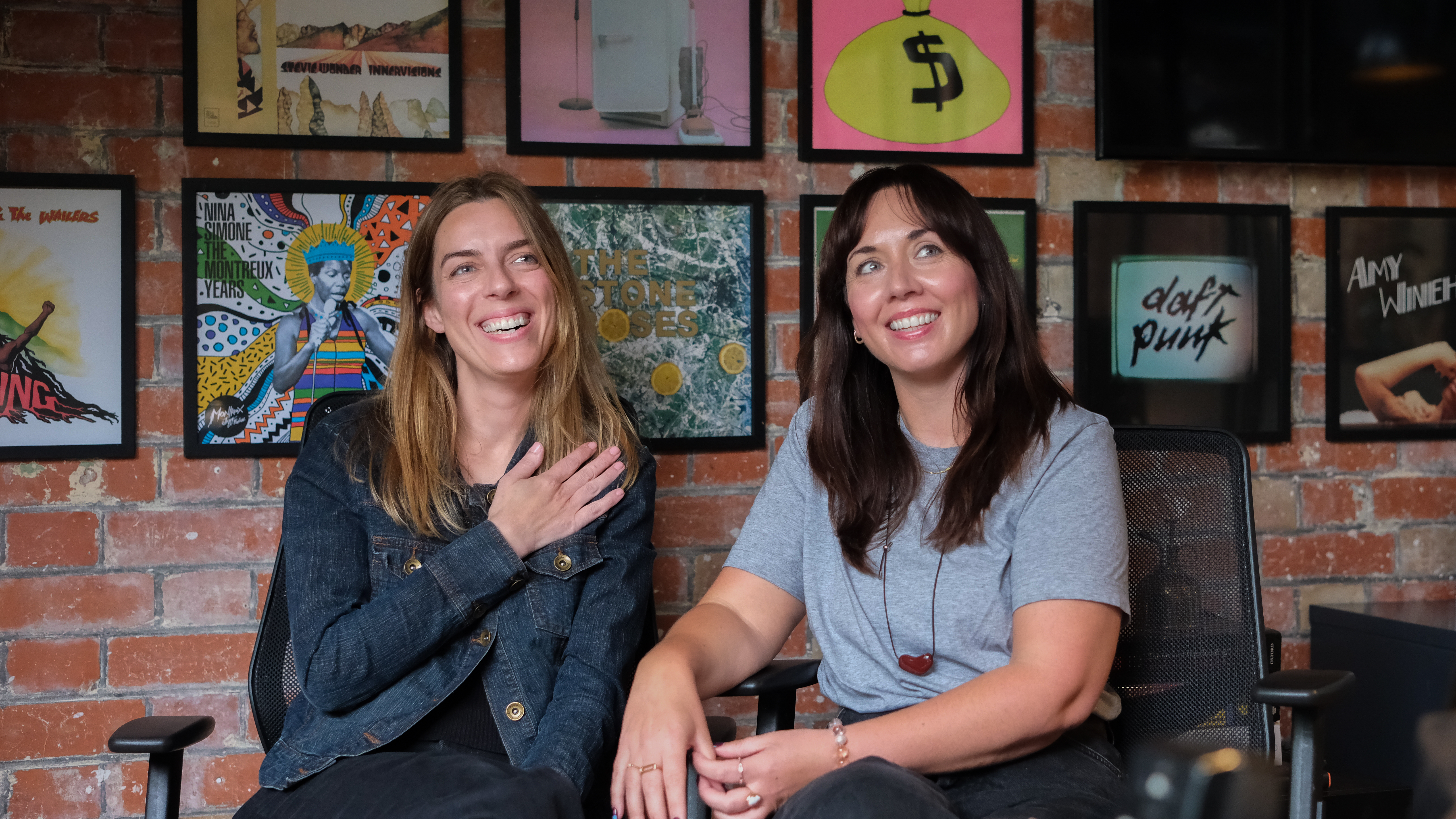 two women smiling with a brick wall covered in artwork behind them