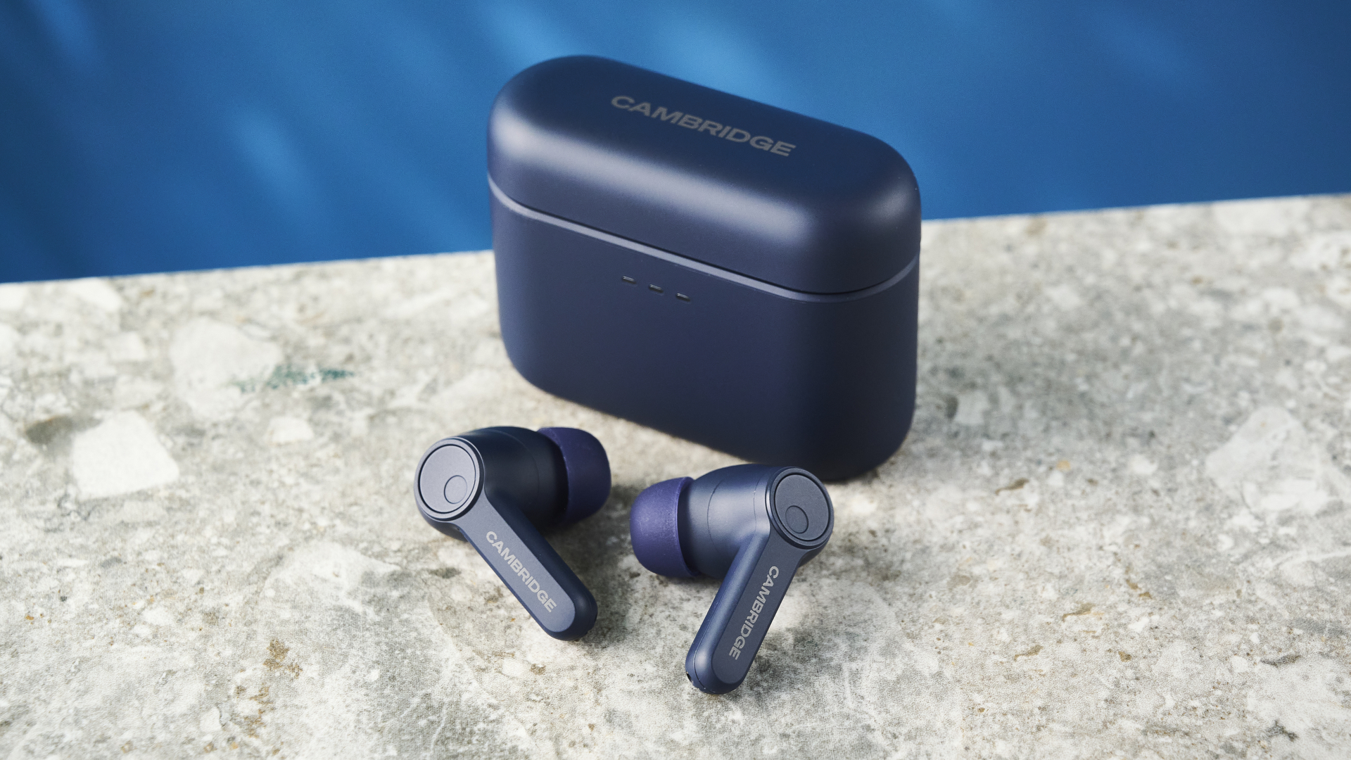 the cambridge audio a100 se earbuds on a blue tom's guide background with a stone-coloured table underneath