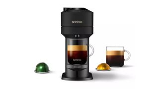 A black Nespresso coffee machine with a coffee cup full of cofffee underneath, another coffee cup to the right and a yellow and green coffee pod on either side