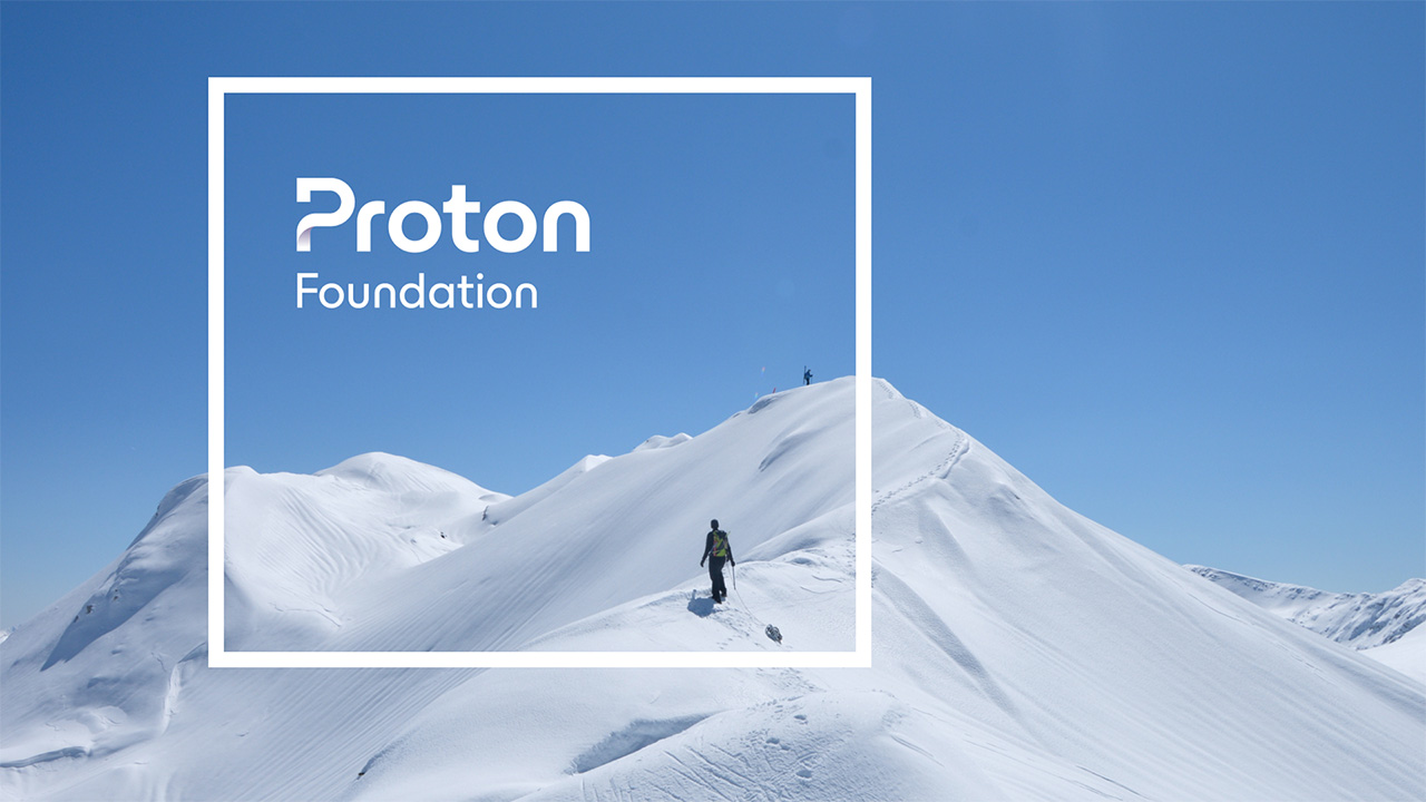 Climber walking across a snowy mountain, in clear blue skies. A white outline of a square box is displayed with the Proton Foundation logo in white text