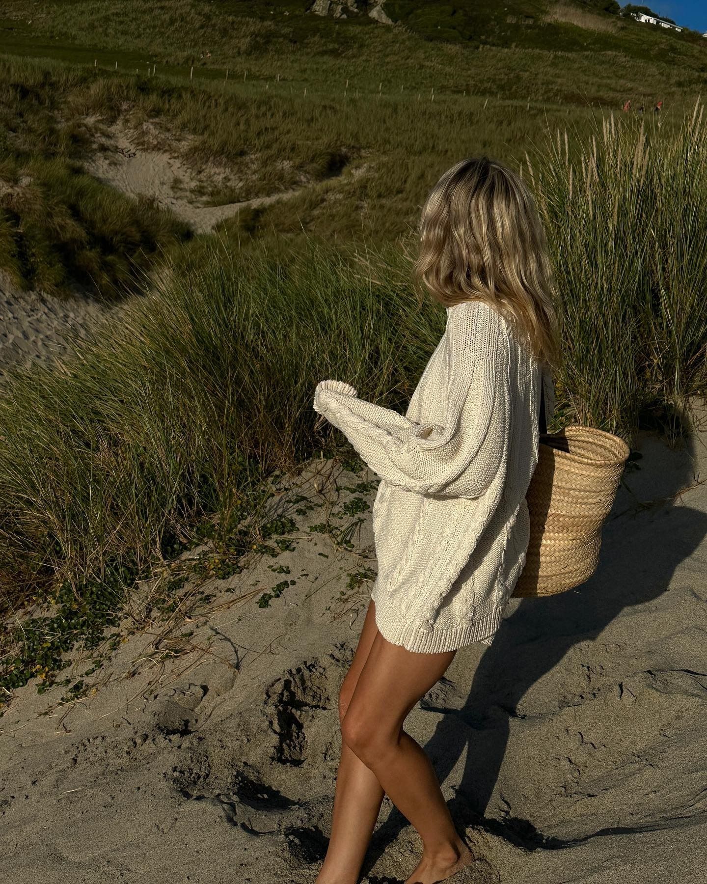 Lucy Williams wearing a cotton loose sweater with a straw bag on the beach.