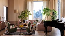 Living room with pale pink walls and a pink corner sofa with patterned armchairs and a grand piano in the corner