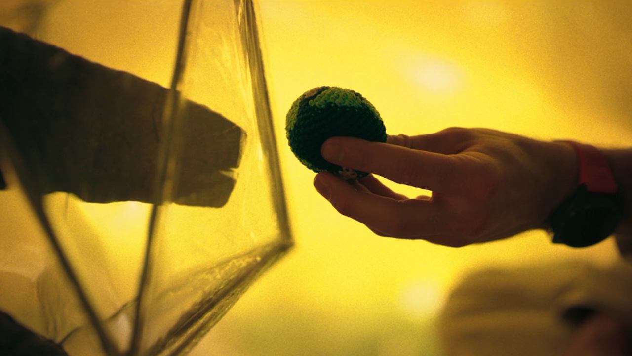 A hand holding an earth toy out to an alien hand in Project Hail Mary