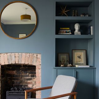 Blue-painted living room with built-in shelves in an alcove and a round mirror above the fireplace