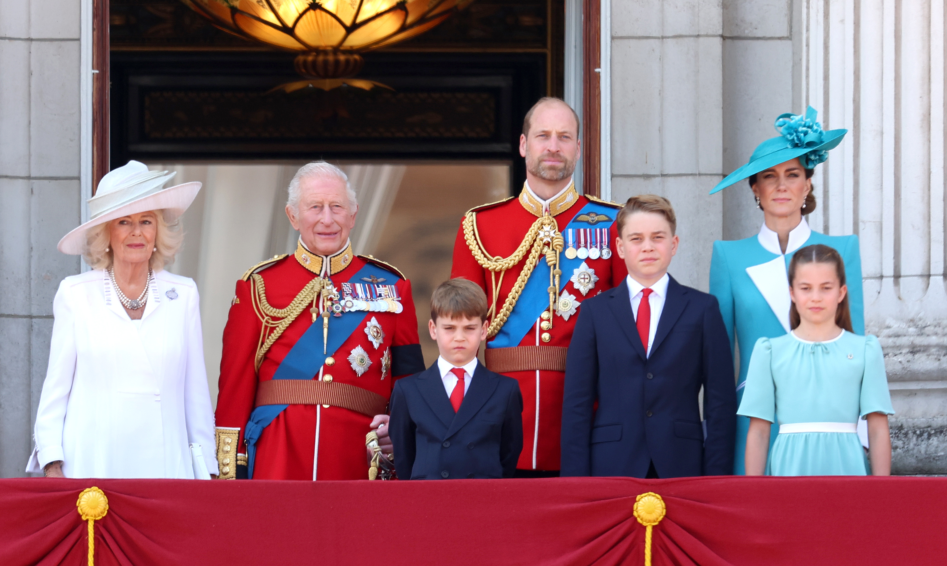 Prince George at Trooping the Colour 2025 wearing a navy suit with a white shirt and a red tie, and joining the Royal Family on the Buckingham Palace balcony