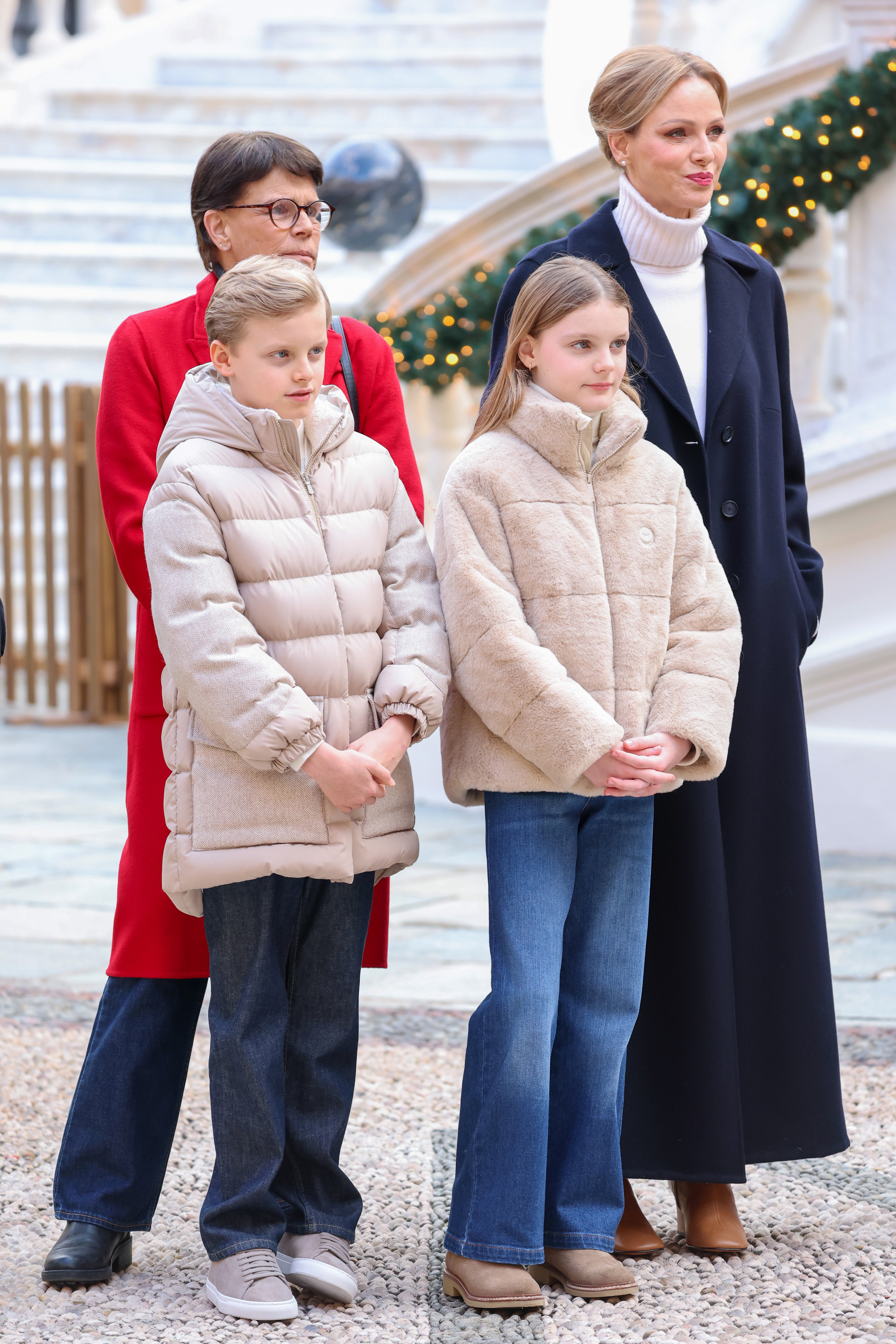 Princess Charlene in a long navy coat standing with Princess Stephanie, Prince Jacques, and Prince Gabriella