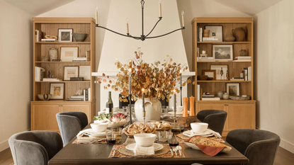 a dining room with two large cabinets on either side filled with decorative objects, a large dining table decorated with plates, bowls, silverware, candles, and a vase of flowers, and chairs on either side
