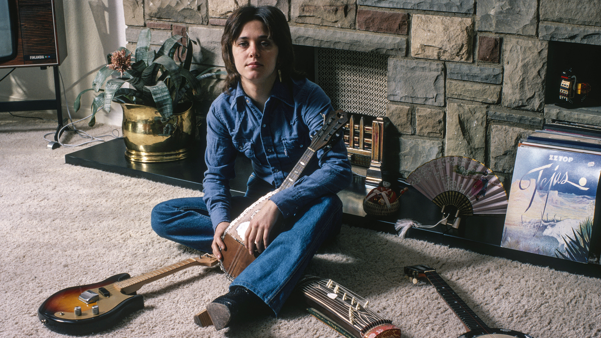 Suzi Quatro with a collection of string instruments, circa 1975. On the right is a copy of ZZ Top's album 'Tejas'.