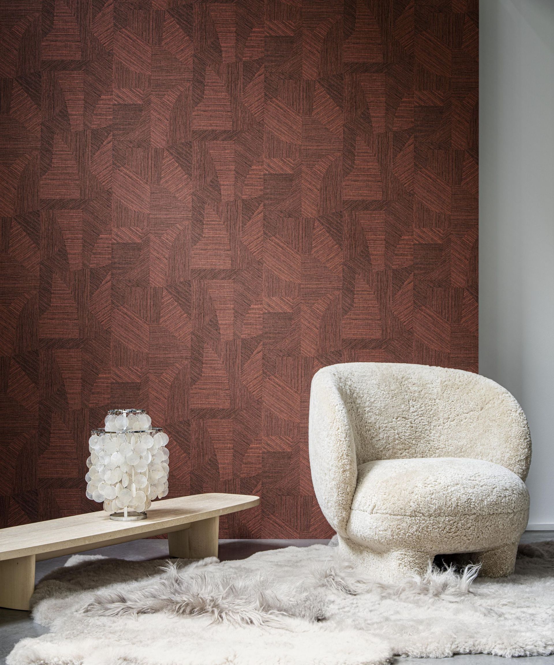Arte's textures grasspaper wallpaper in a deep red shade with a small white armchair in front of it and a sheepskin rug