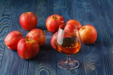 Apples and a glass of brown spirit on a wooden counter