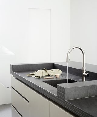 A modern kitchen island with black Vermont worktop and a raised area behind the sink