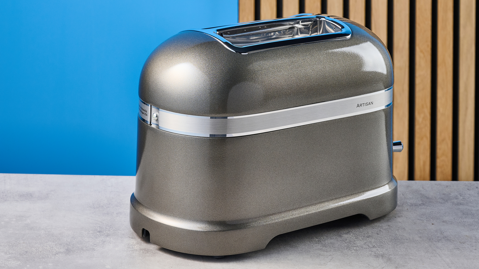A photograph of the KitchenAid Pro Line toaster on a stone work surface with a blue and wooden background
