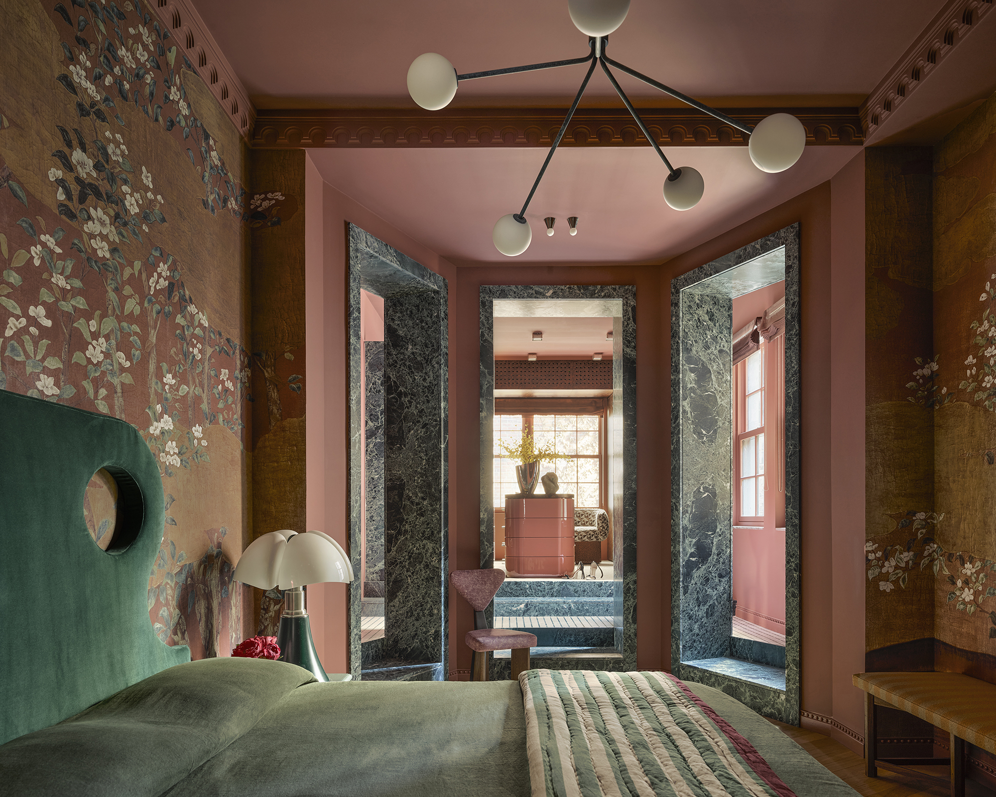 wallpapered bedroom with abstract green headboard looking on to a marble-clad dressing room