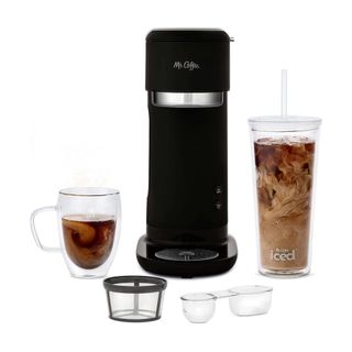 Black iced coffee maker with tumbler full of iced coffee, filters, scoop and glass mug with coffee in