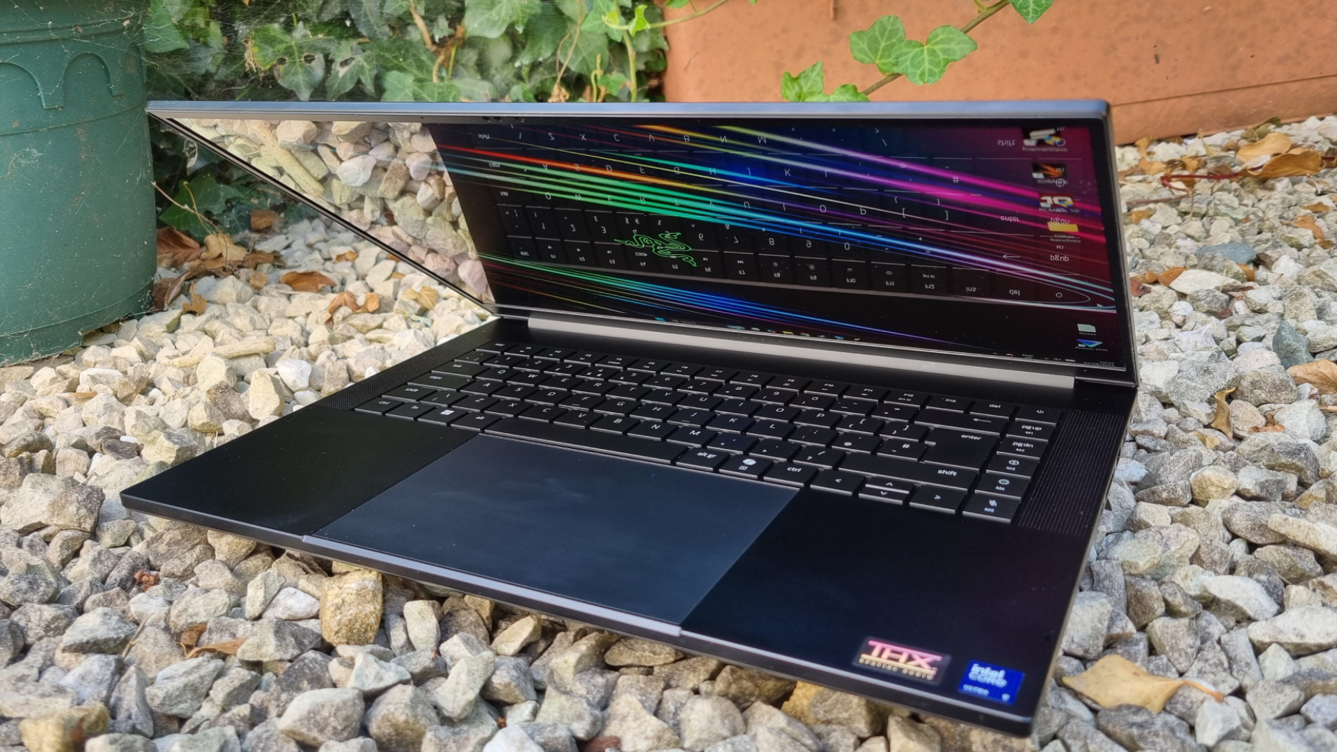 A Razer Blade 16 gaming laptop on white gravel, with its screen tilted