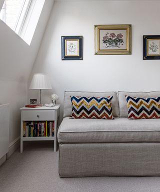 A bedroom with a grey sofa bed and zig zag patterned cushions, sloping eaves and dormer window.
