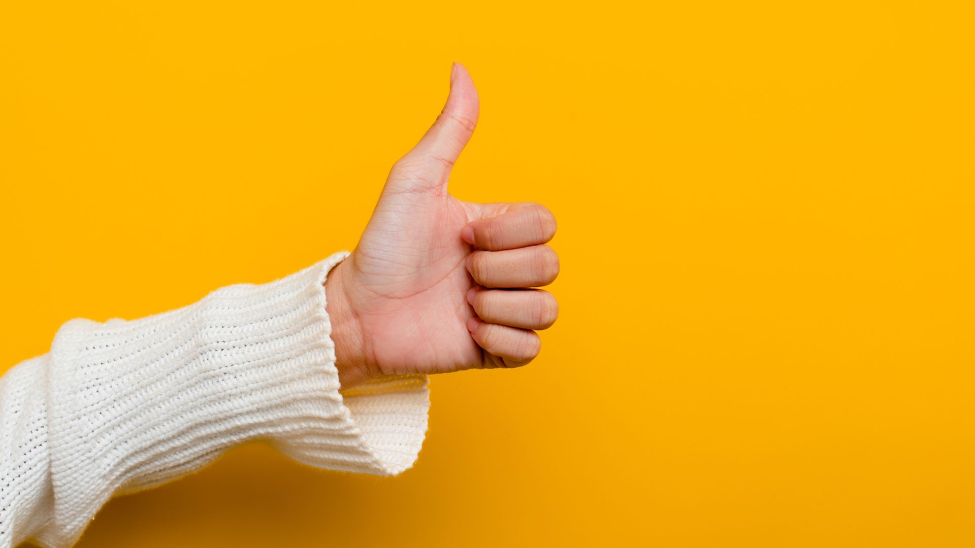 A woman's hand in a thumbs-up gesture against a yellow background.