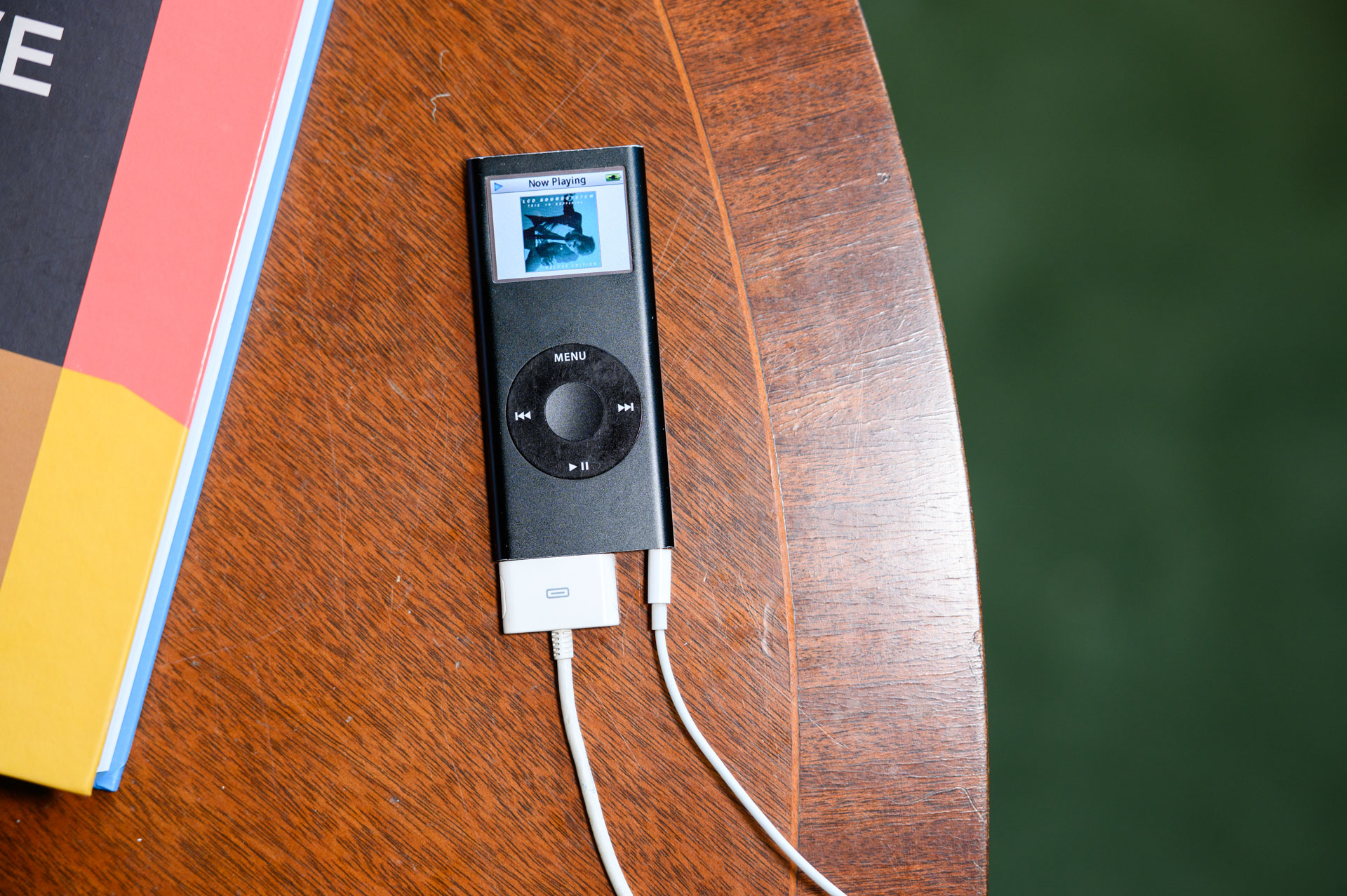 Black iPod Nano 2006 8GB model from above on a mahogany table, alongside a colorful book