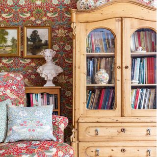 room with wooden cabinet, patterned armchair and wallpaper and white bust