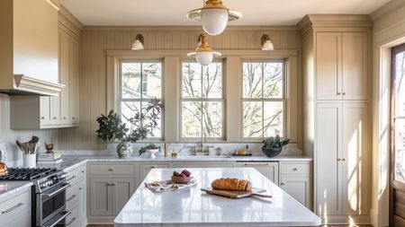 A large L-shaped kitchen with an island, wall paneling, and a sink beneath the window