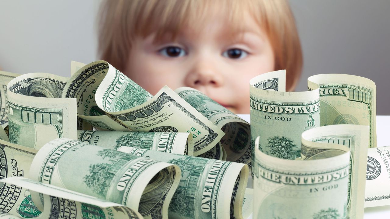 picture of one hundred dollar bills on a table with a young child peering over it in the background