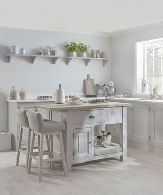 A gray kitchen with a freestanding kitchen island with built-in pet bed with a dog on it and kitchen cabinets around ir