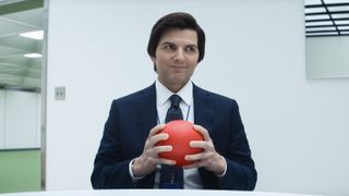 Adam Scott wearing a suit and holding a red ball as Mark Scout in Severance.