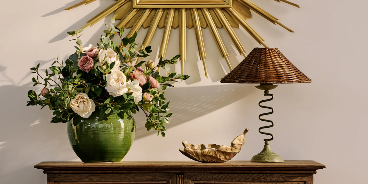 A credenza with a vase of flowers, a leaf-shaped bowl, and a table lamp with a wiggly base
